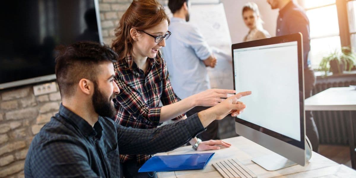 A man and a woman pointing at a computer screen while discussing something at a desk.