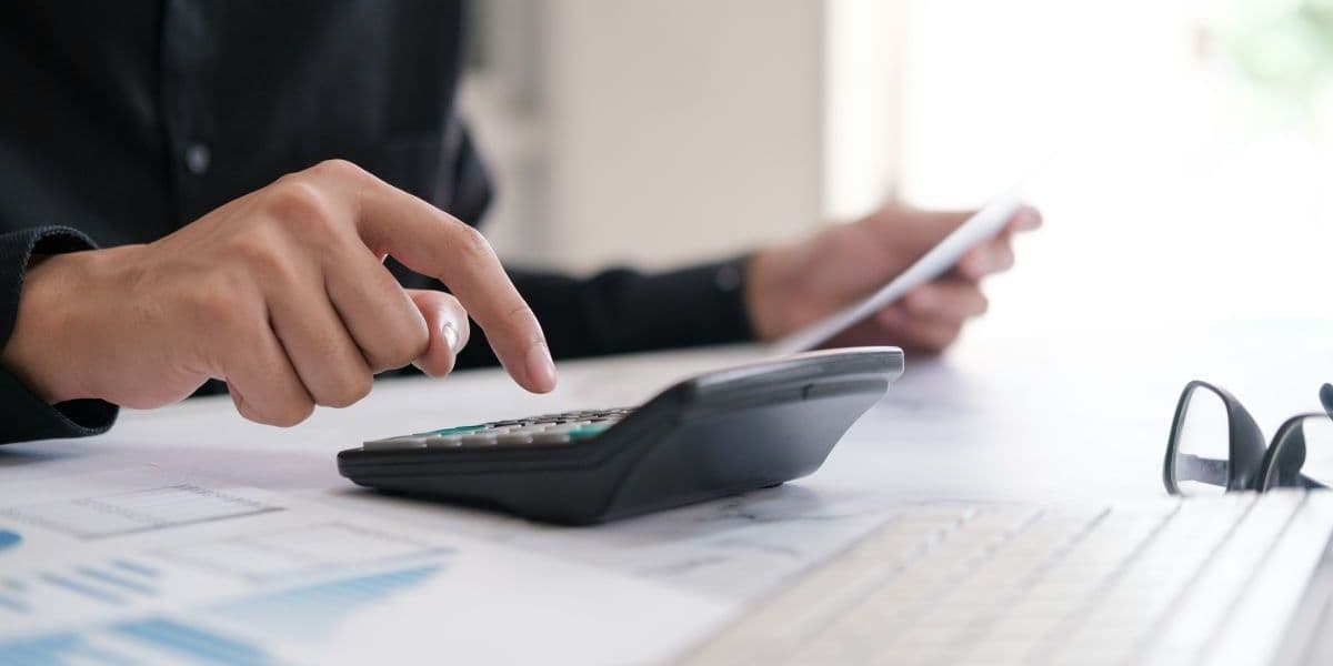 Office worker using calculator and laptop to plan budget and career finances.